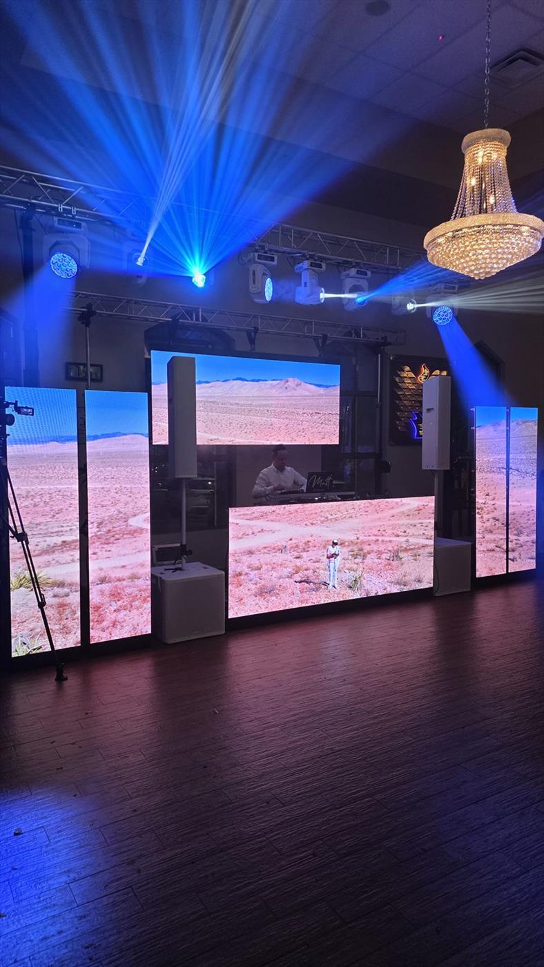 A large LED video wall lit by blue moving-head beams under a chandelier