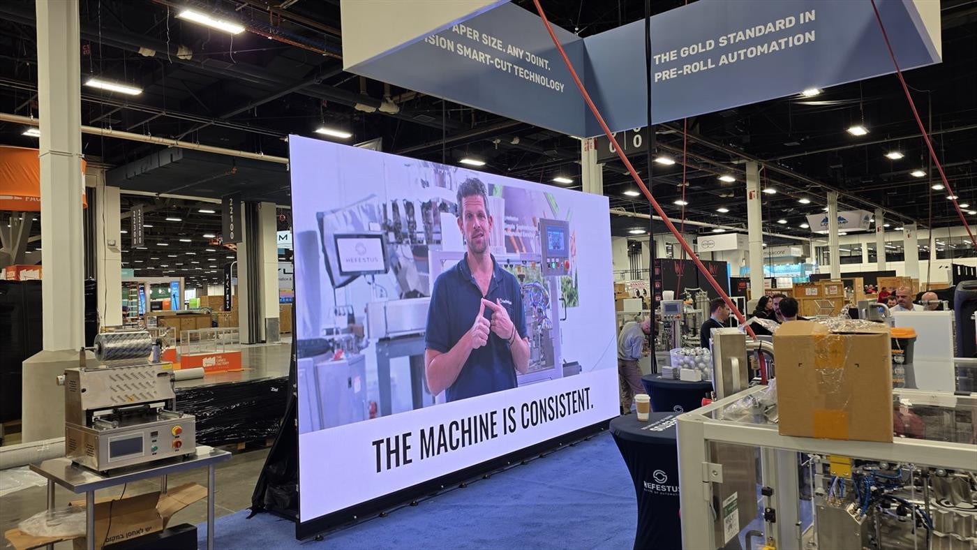 A large LED video wall in a brightly lit convention hall trade show booth